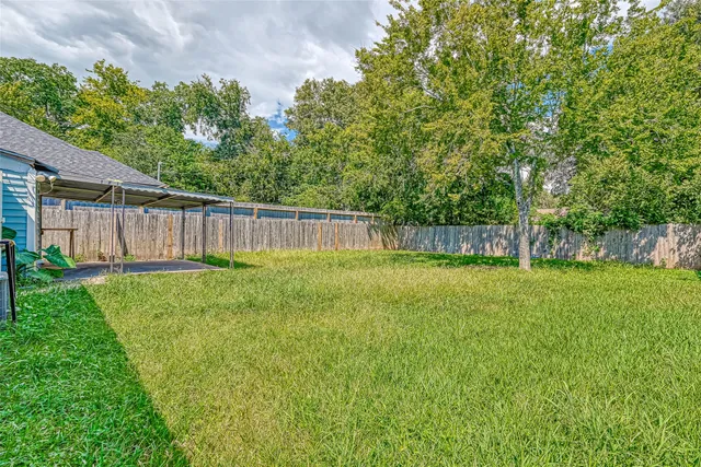 a view of a backyard with large trees and wooden fence
