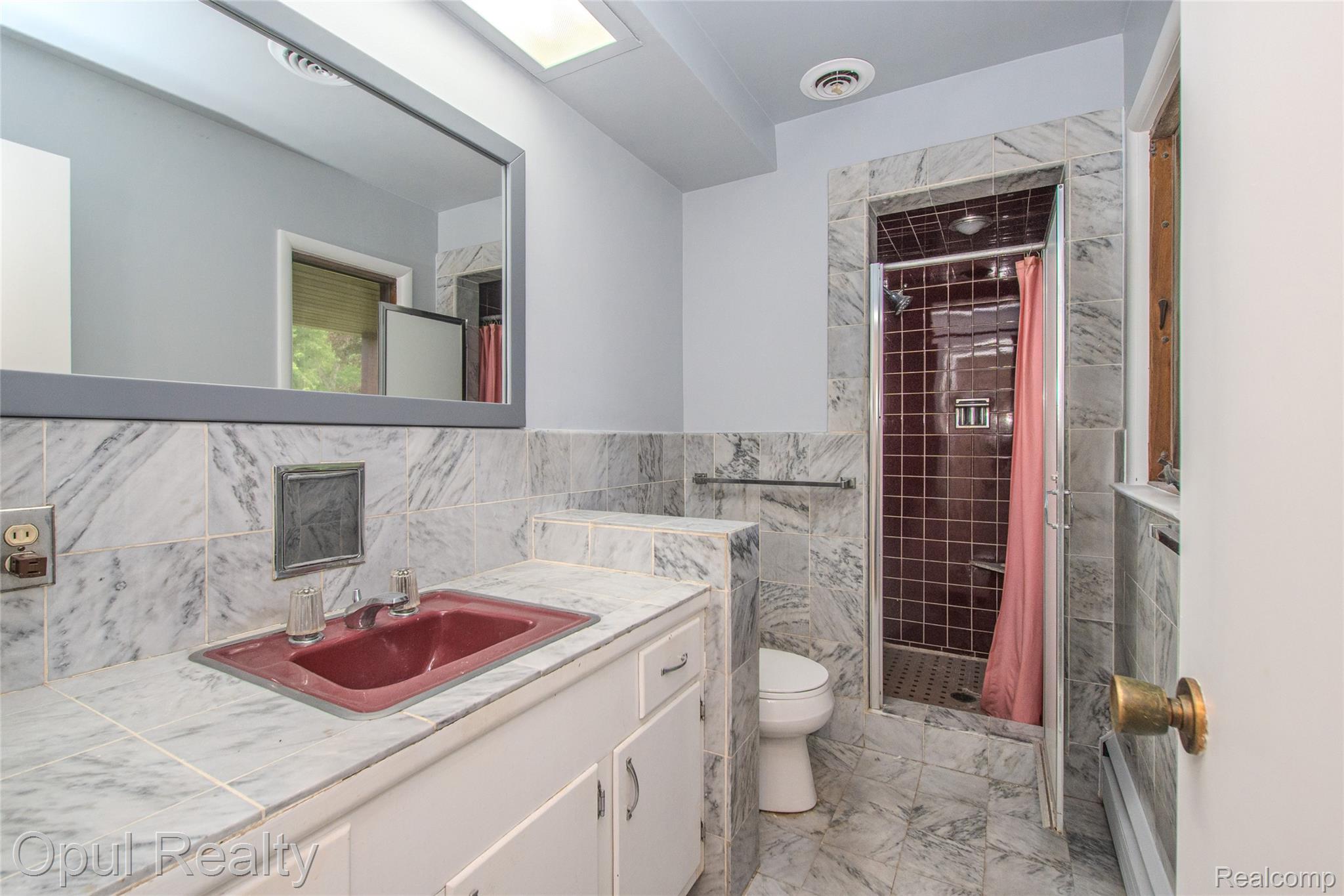 6455 Norham Road Bloomfield Hills, MI 48301 - Photo 27 of 93 Bathroom featuring full marble-look tile flooring and wainscoting, an integrated red basin, a matching vanity with white cabinetry, and a glass-enclosed shower with brown tiled walls