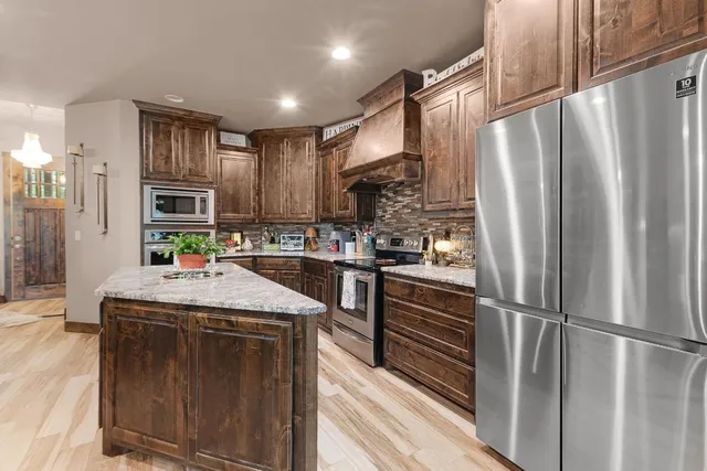 a kitchen with stainless steel appliances granite countertop a stove a sink dishwasher a refrigerator white cabinets and wooden floor