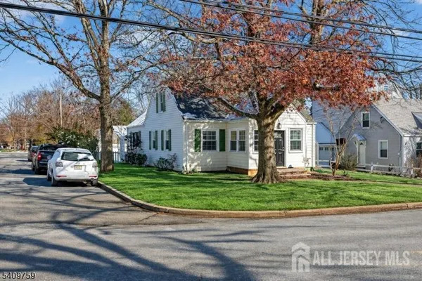 a view of a white house in front of a big yard with large trees