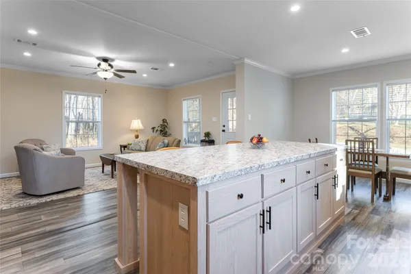 a open kitchen with granite countertop a stove a sink a dining table and chairs with wooden floor