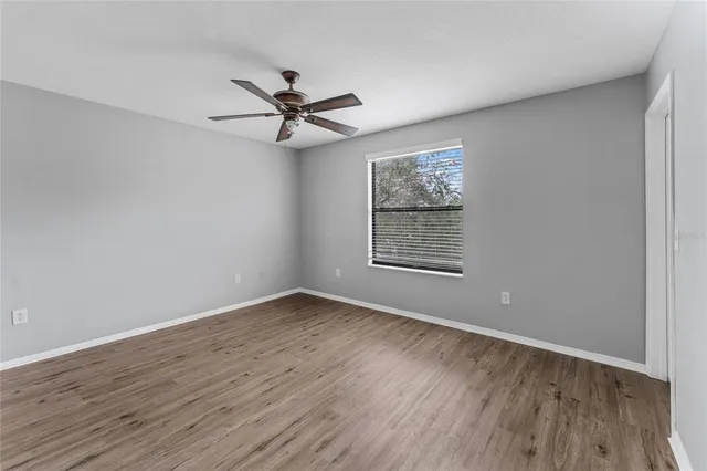 an empty room with wooden floor a ceiling fan and windows