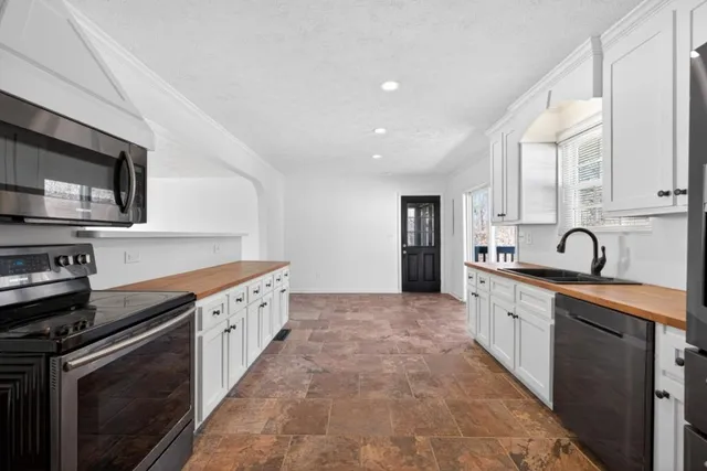 a large kitchen with stainless steel appliances granite countertop a stove a sink dishwasher and a microwave oven with white cabinets