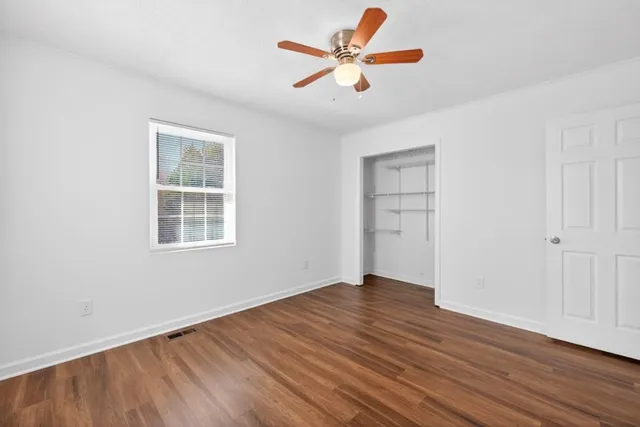 an empty room with wooden floor chandelier fan and windows