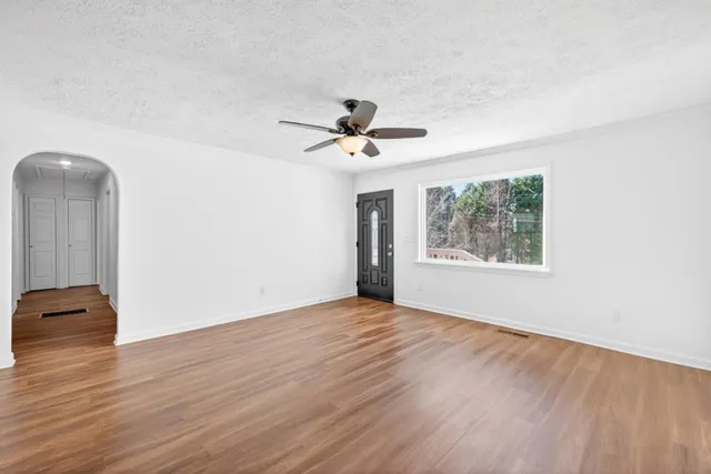an empty room with wooden floor chandelier fan and windows