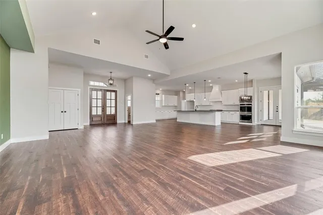 a view of an empty room and kitchen view with wooden floor