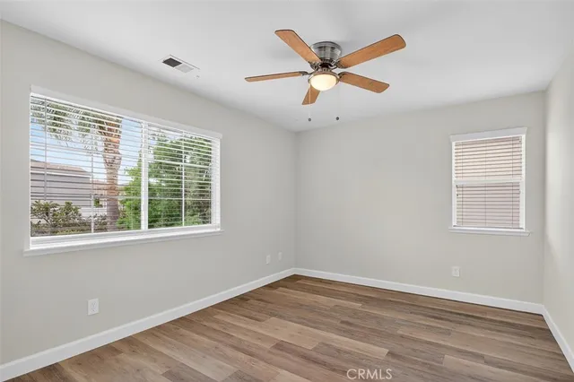 a view of an empty room with wooden floor and a ceiling fan