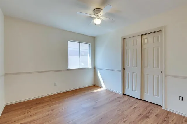 an empty room with wooden floor chandelier fan and windows
