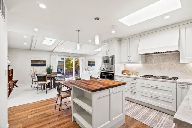 a kitchen with stainless steel appliances kitchen island granite countertop a stove top oven a sink dishwasher a dining table and chairs with wooden floor