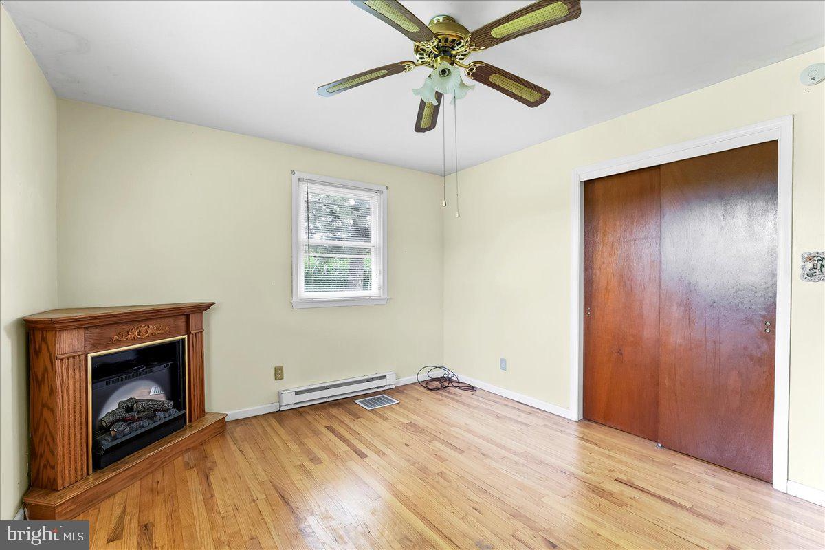 374 Street Road Cochranville, PA 19330 - Photo 13 of 28 an empty room with wooden floor a ceiling fan and a fireplace