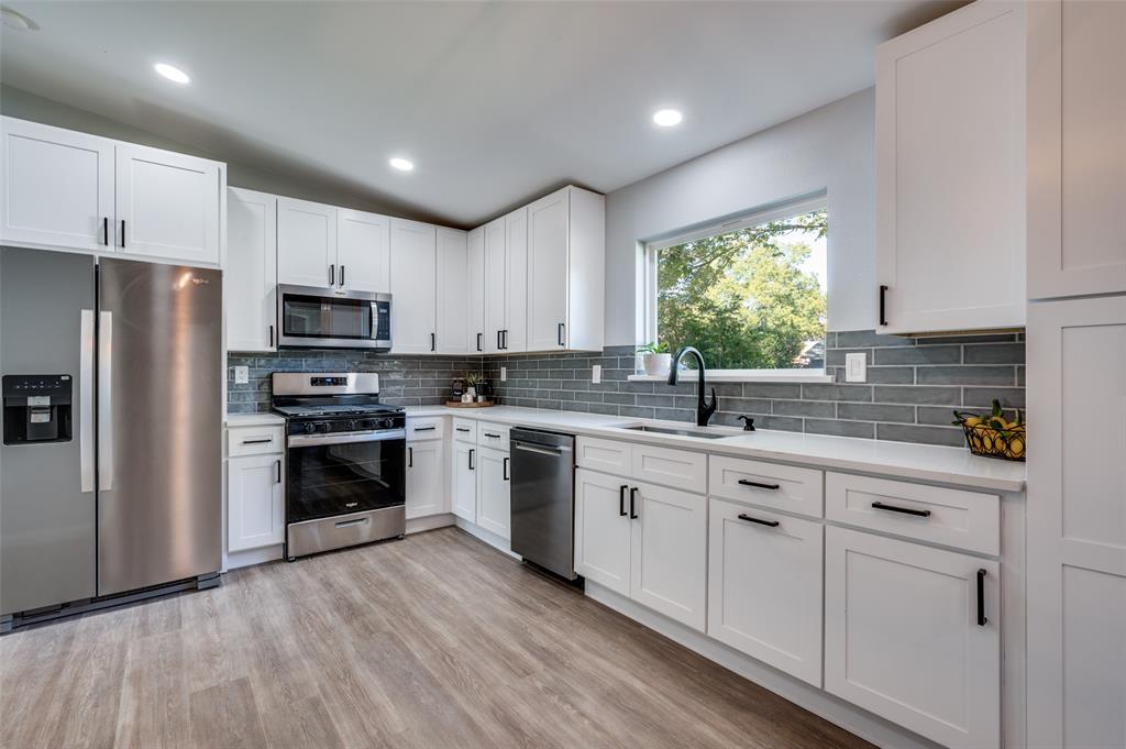 a kitchen with kitchen island granite countertop white cabinets a sink a window and stainless steel appliances