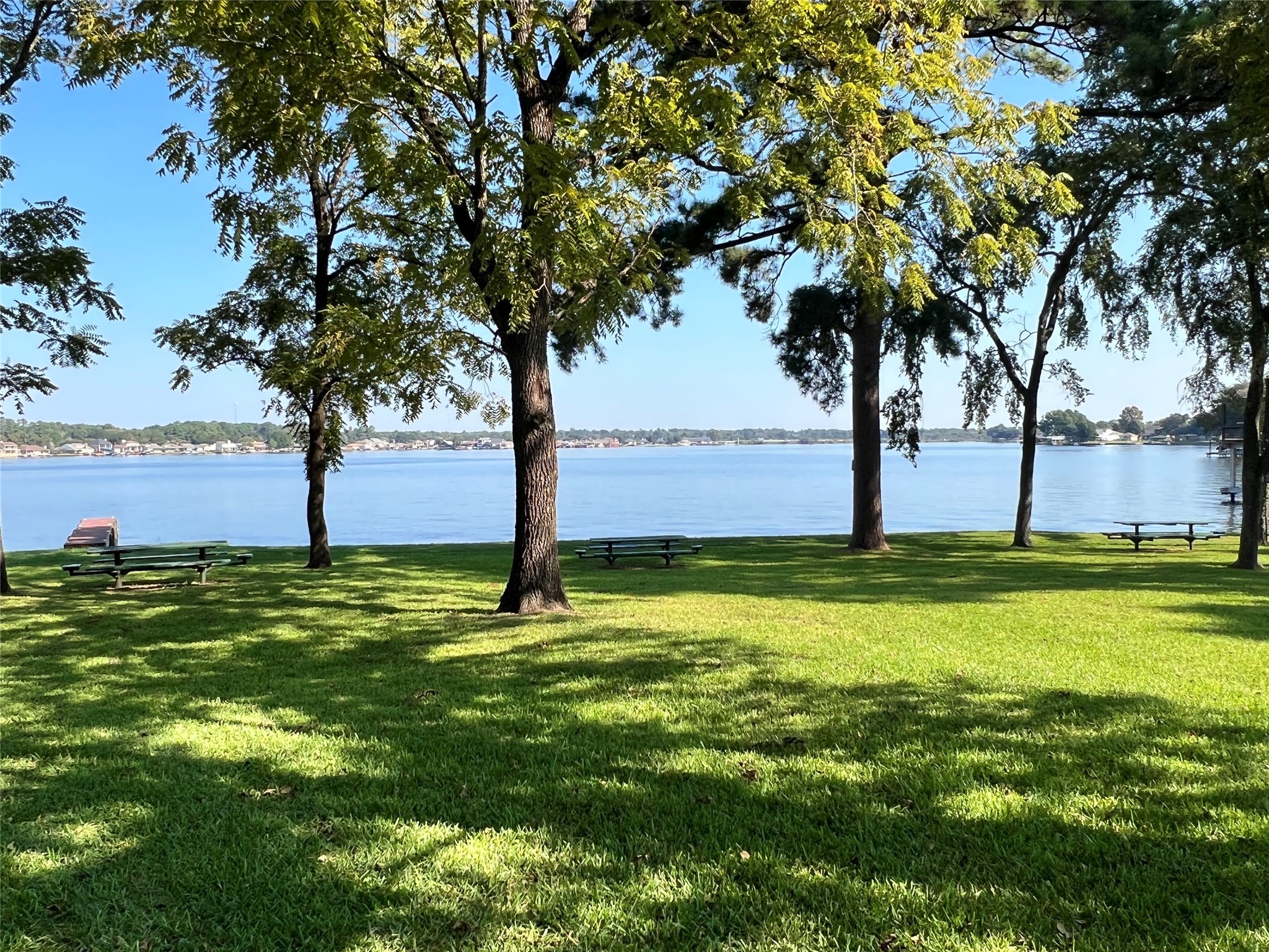 12121 North Ridgeway Willis, TX 77318 - Photo 21 of 47 This photo showcases neighborhood 7ac park with serine lakeside view with lush green grass and mature trees providing shade. There are picnic tables scattered across the area, perfect for outdoor relaxation and enjoying the tranquil water scenery.