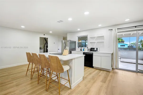 a kitchen with stainless steel appliances kitchen island granite countertop a stove a sink a refrigerator and white cabinets with wooden floor