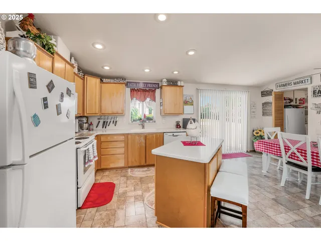 a kitchen with stainless steel appliances kitchen island granite countertop a refrigerator a sink dishwasher and a dining table with wooden floor