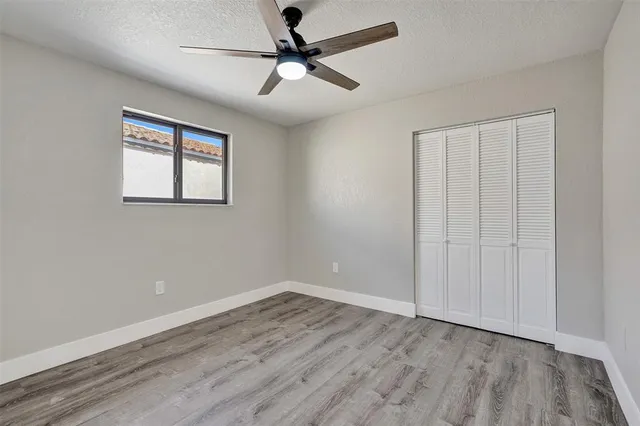 an empty room with wooden floor ceiling fan and windows
