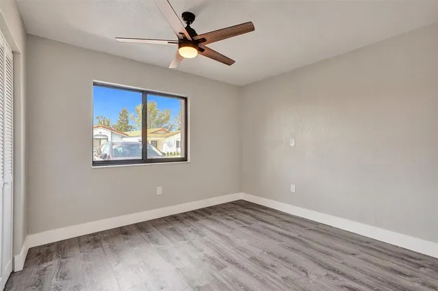 an empty room with wooden floor ceiling fan and window