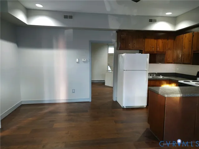 a view of a refrigerator in kitchen and an empty room with wooden floor