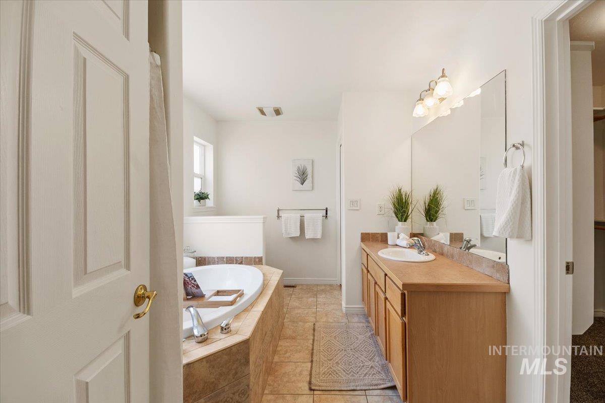 2032 Talus Loop Twin Falls, ID 83301 - Photo 33 of 43 Bathroom featuring a built-in soaking tub with tile surround, a single vanity with wood cabinetry and an integrated sink, a large wall-mounted mirror, and tile flooring