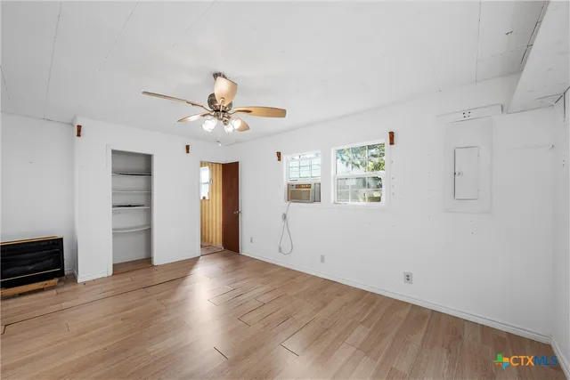 an empty room with wooden floor chandelier fan and windows
