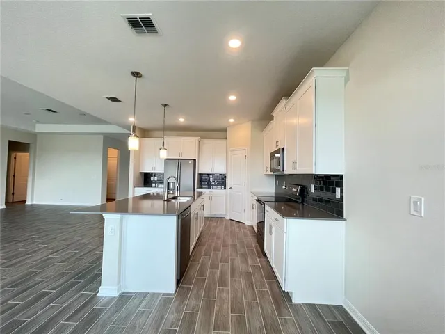 a kitchen with stainless steel appliances a stove top oven a sink a refrigerator white cabinets and wooden floor