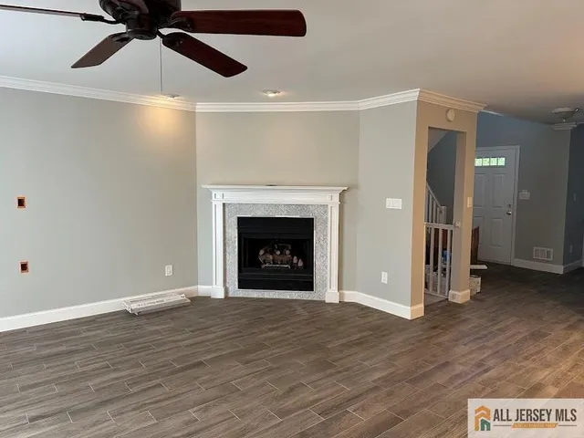 a view of an empty room with wooden floor a ceiling fan and a fireplace