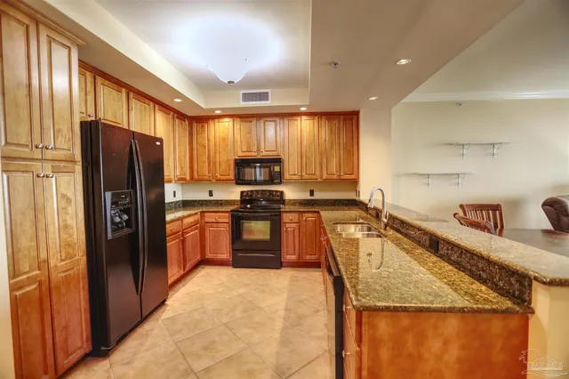 a kitchen with granite countertop a refrigerator a sink a stove top oven and cabinets