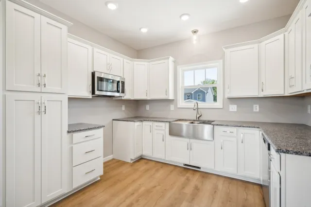 a kitchen with granite countertop white cabinets appliances a sink and a window