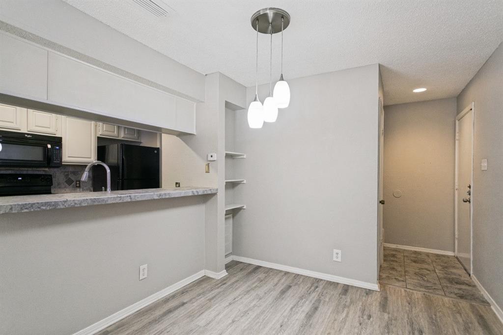 18240 Midway Road, Unit 905 Dallas, TX 75287 - Photo 16 of 29 Wood-finish flooring, kitchen pass-through with stone-look countertop, white upper and lower cabinetry, built-in shelving, and a three-light pendant fixture