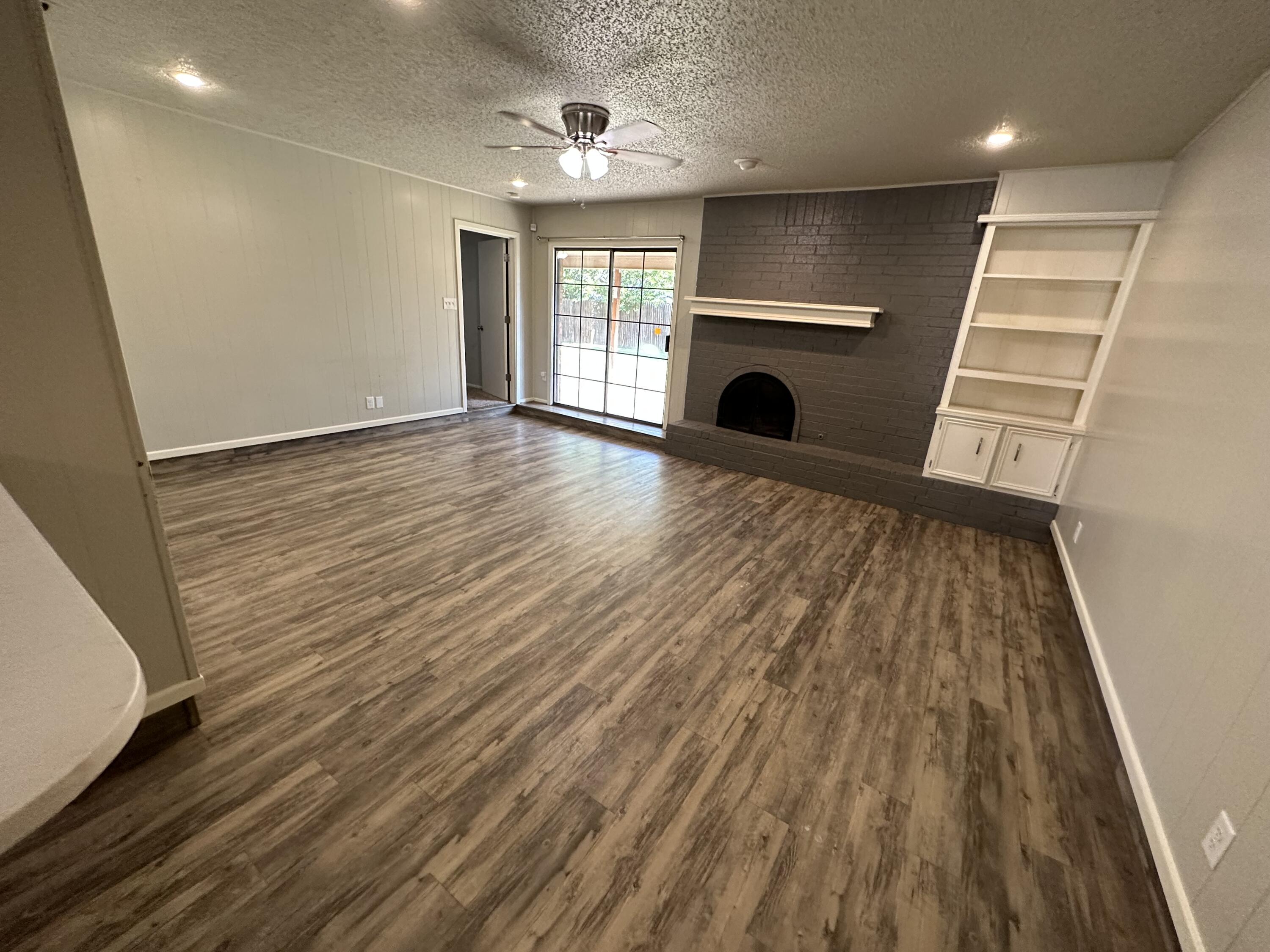 4804 71st Street Lubbock, TX 79424 - Photo 5 of 14 an empty room with wooden floor a fireplace and windows