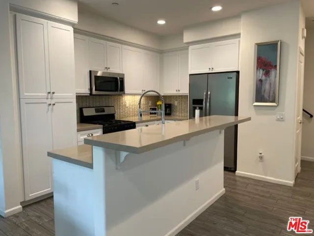 a kitchen with stainless steel appliances a sink a stove a microwave a refrigerator a sink and white cabinets