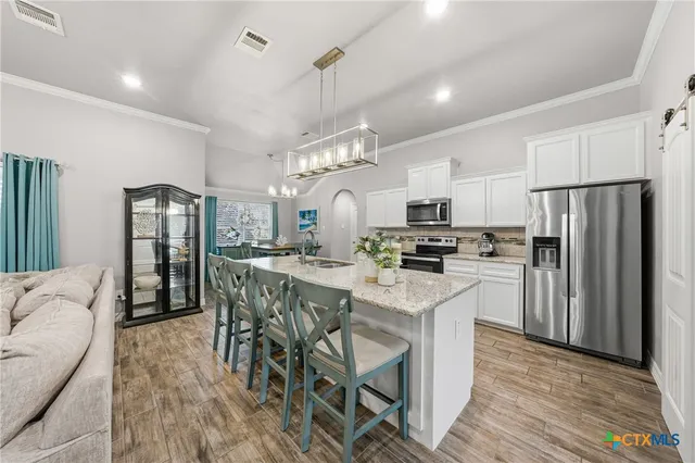 a kitchen with stainless steel appliances a refrigerator a stove a sink a dining table and chairs with wooden floor