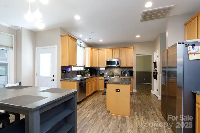 a kitchen with stainless steel appliances kitchen island granite countertop a stove refrigerator and cabinets