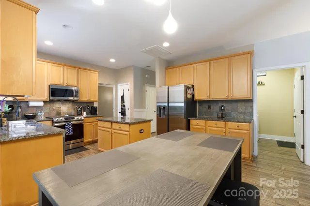 a large kitchen with stainless steel appliances granite countertop a stove a sink a refrigerator and white cabinets with wooden floor