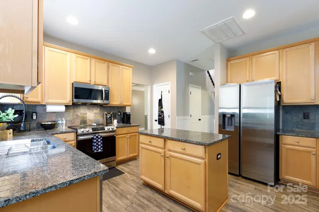 a kitchen with stainless steel appliances granite countertop a refrigerator a stove and a sink with wooden floor