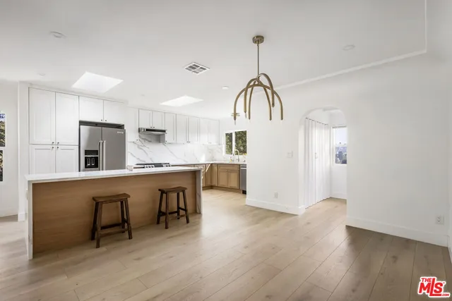 a kitchen with kitchen island stainless steel appliances a table chairs refrigerator sink and cabinets