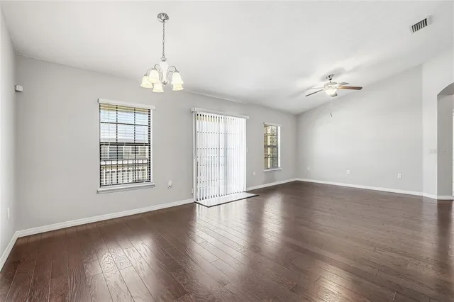 an empty room with wooden floor chandelier fan and windows