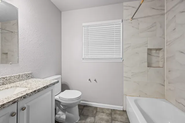 a bathroom with a granite countertop toilet a sink a mirror and a bathtub