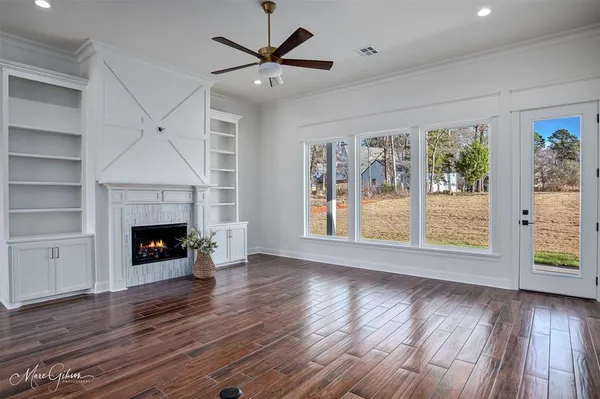 a view of an empty room with wooden floor fireplace and a window
