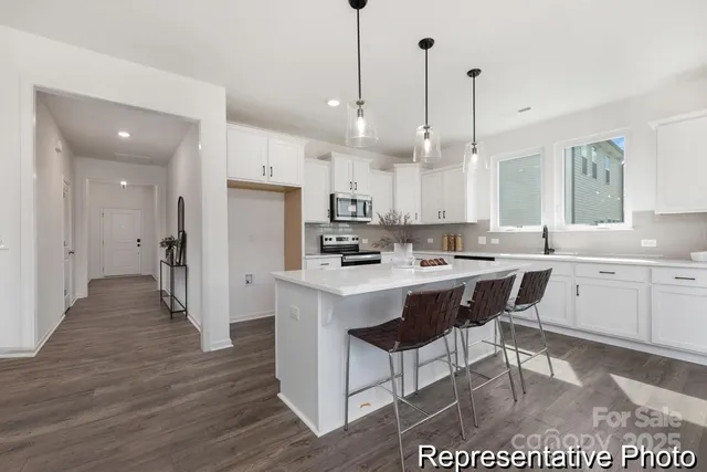 a kitchen with stainless steel appliances kitchen island granite countertop a sink a stove a refrigerator and white cabinets with wooden floor