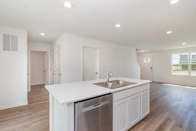 a kitchen with a sink dishwasher and white cabinets with wooden floor