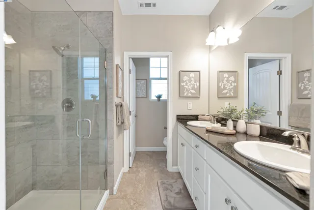 a bathroom with a granite countertop double vanity sink a mirror and shower