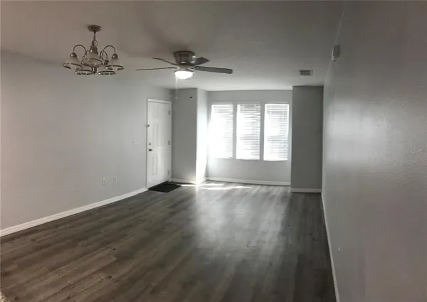 an empty room with wooden floor chandelier fan and windows
