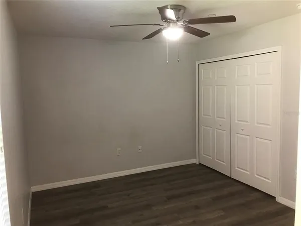 an empty room with wooden floor closet and fan