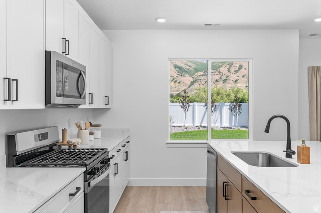 1352 West 2350 South, Unit 18 Perry, UT 84302 - Photo 8 of 26 Modern kitchen featuring white cabinetry with matte black hardware, stainless steel appliances, and light-toned wood-finish flooring