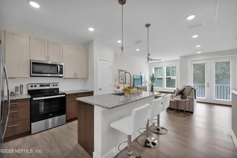 a kitchen with kitchen island a stove a counter top space a sink cabinets and living room view