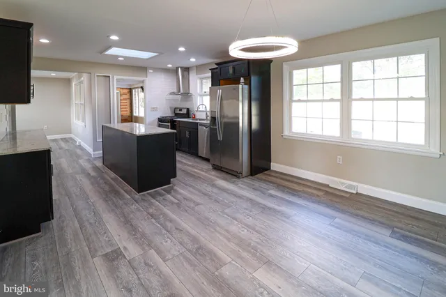a view of kitchen with stainless steel appliances granite countertop a refrigerator a sink dishwasher a stove and a dining table with wooden floor