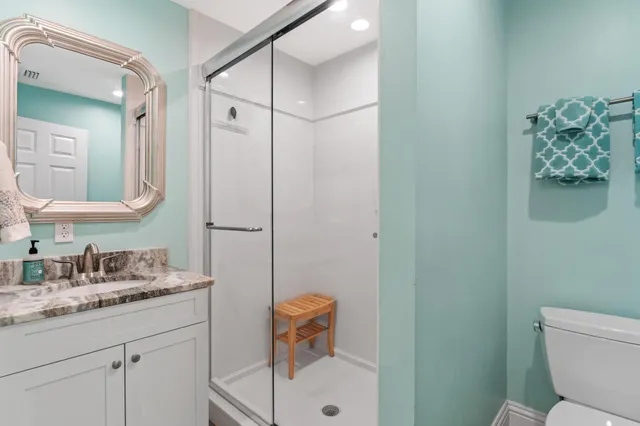 a bathroom with a granite countertop sink a toilet a shower and mirror