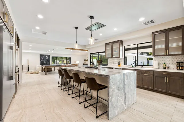 a kitchen with stainless steel appliances kitchen island granite countertop a table chairs sink and cabinets