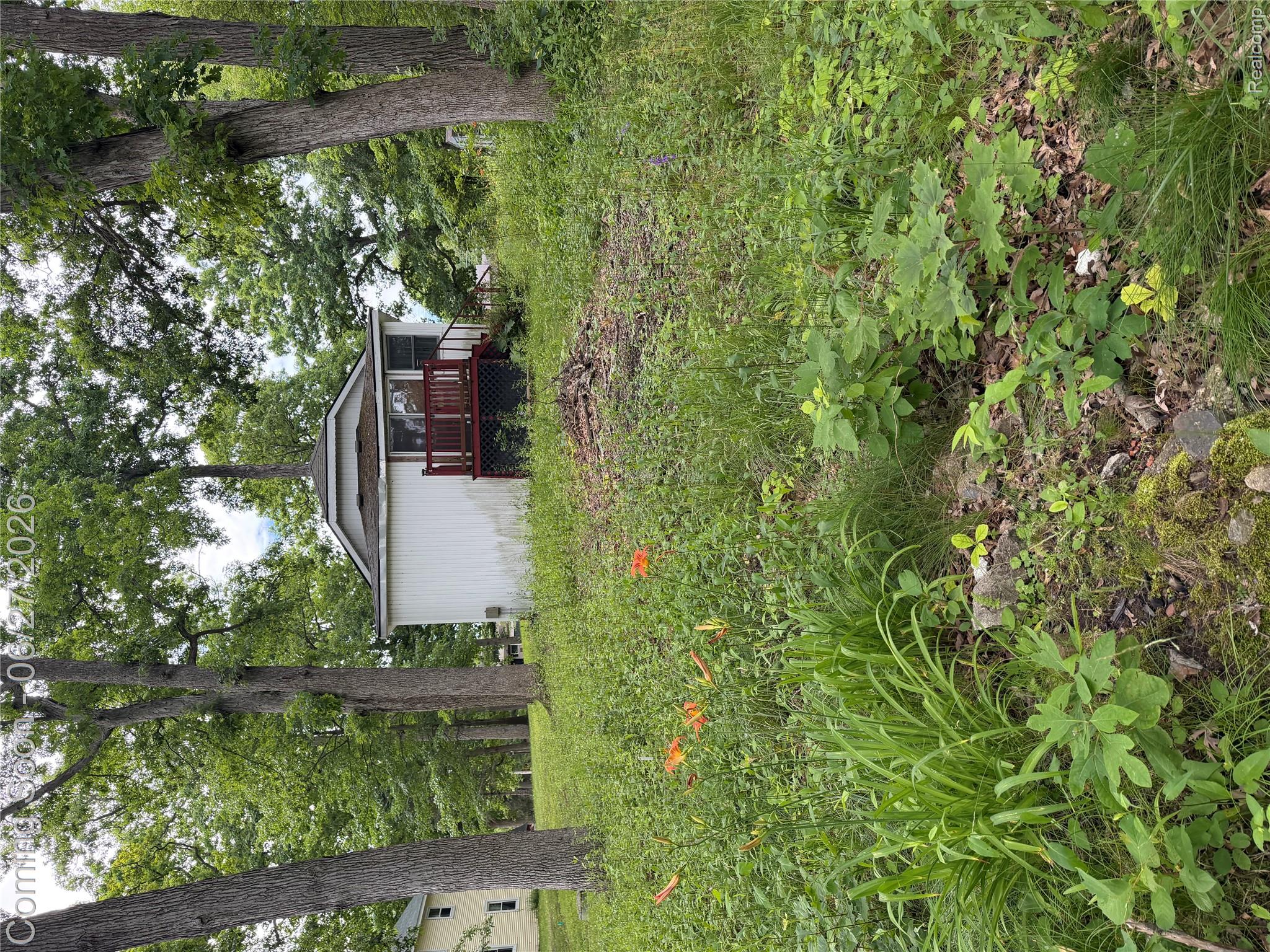White siding residence featuring a red-stained deck with railing, an octagonal roofline, and surrounding mature trees