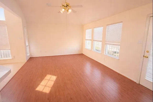 an empty room with wooden floor fan and windows